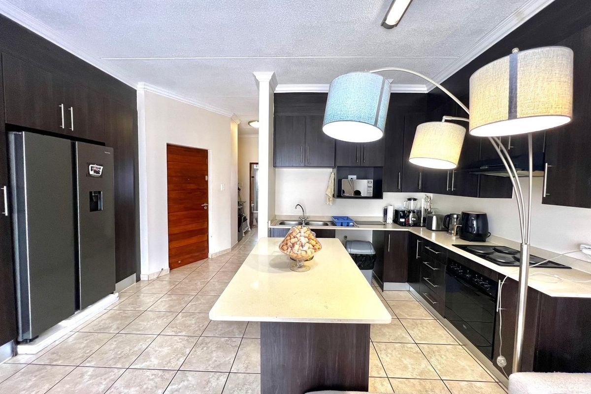 Modern kitchen featuring dark wood cabinetry, stone countertops, a central island, and integrated appliances, finished with neutral floor tiles.
