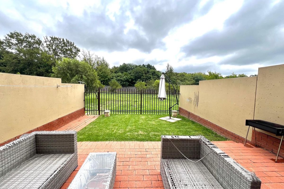 A private rear courtyard featuring brick paving, a small lawn area, and secure boundary walls with metal fencing overlooking a green space.