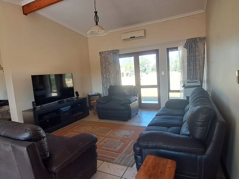 Spacious living room featuring vaulted ceilings with exposed timber beams, tiled flooring, and direct access to the outdoor area via double glass doors.