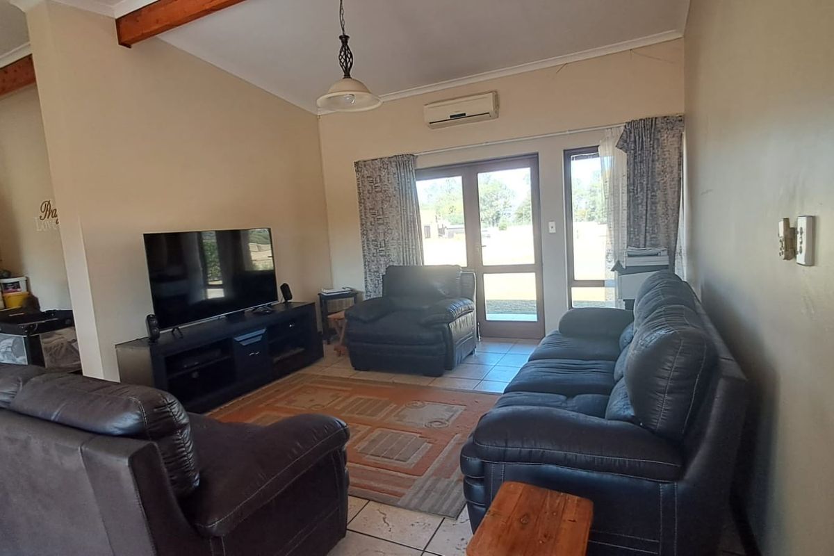 Spacious living room featuring vaulted ceilings with exposed timber beams, tiled flooring, and direct access to the outdoor area via double glass doors.