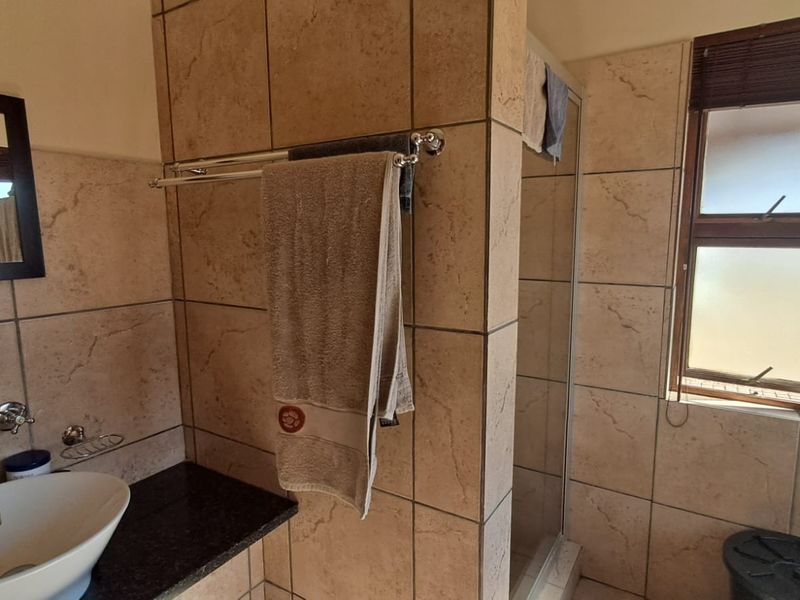 A functional bathroom featuring a vessel sink on a granite vanity, tiled walls, and a separate shower enclosure with natural light.