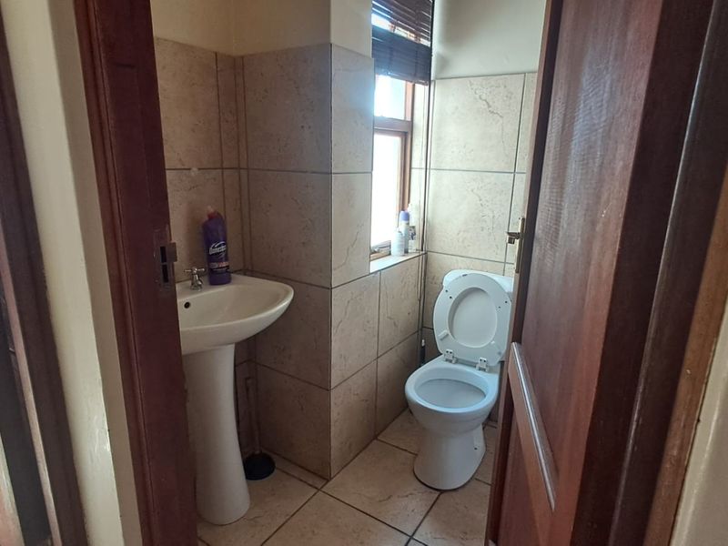 A compact bathroom featuring a pedestal basin, toilet, and neutral floor-to-ceiling wall tiling.