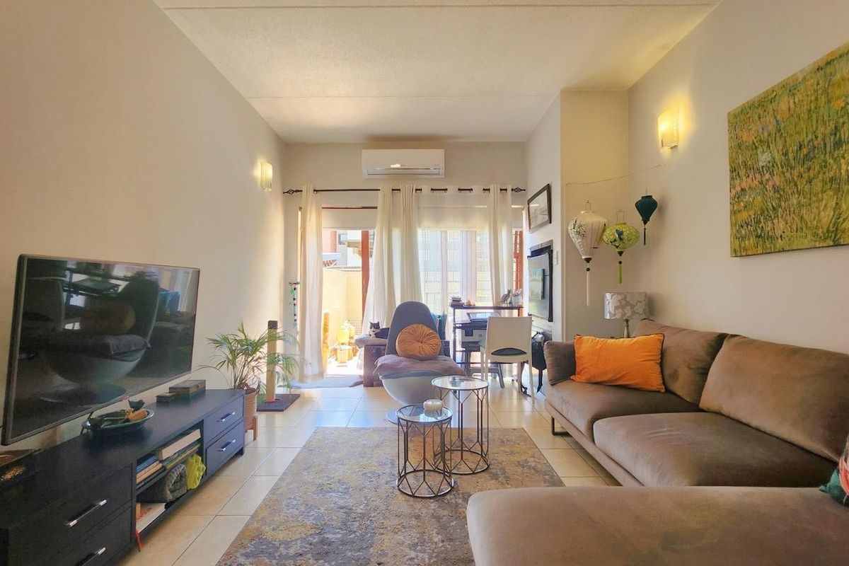 A comfortable living room featuring tiled flooring, wall-mounted lighting, and a split-system air conditioner, with direct access to an outdoor area.
