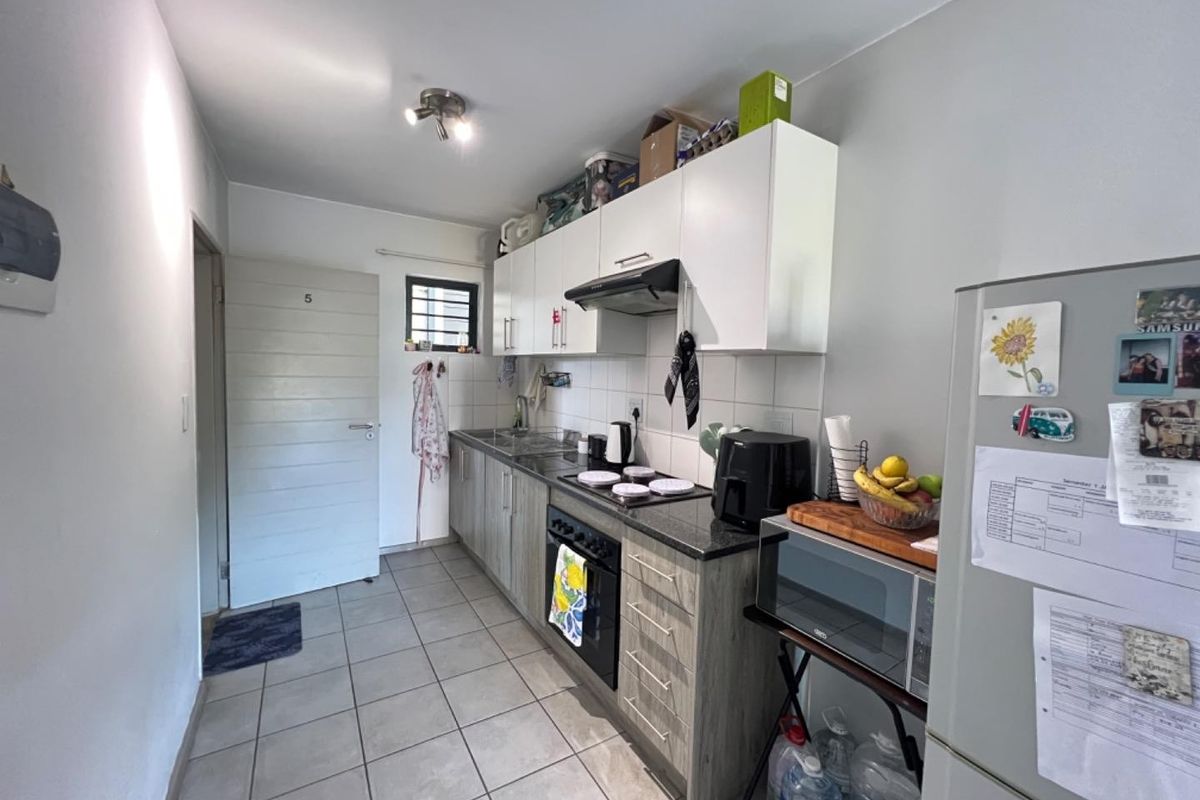 A functional galley-style kitchen featuring modern two-tone cabinetry, a built-in oven with hob, extractor fan, and tiled flooring throughout.