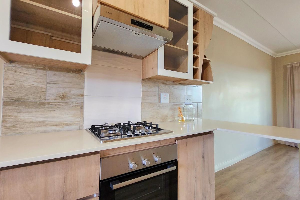 Modern kitchen featuring light wood-finish cabinetry, stone countertops, a built-in gas hob, oven, and extractor fan with a stylish tiled backsplash.