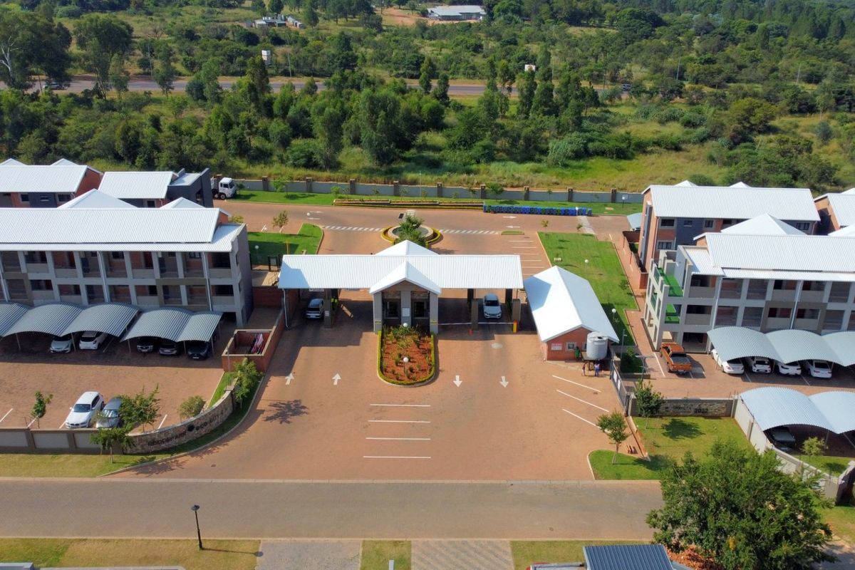 Aerial view of a modern apartment complex featuring a secure gated entrance, paved driveway, and multiple carport parking structures.