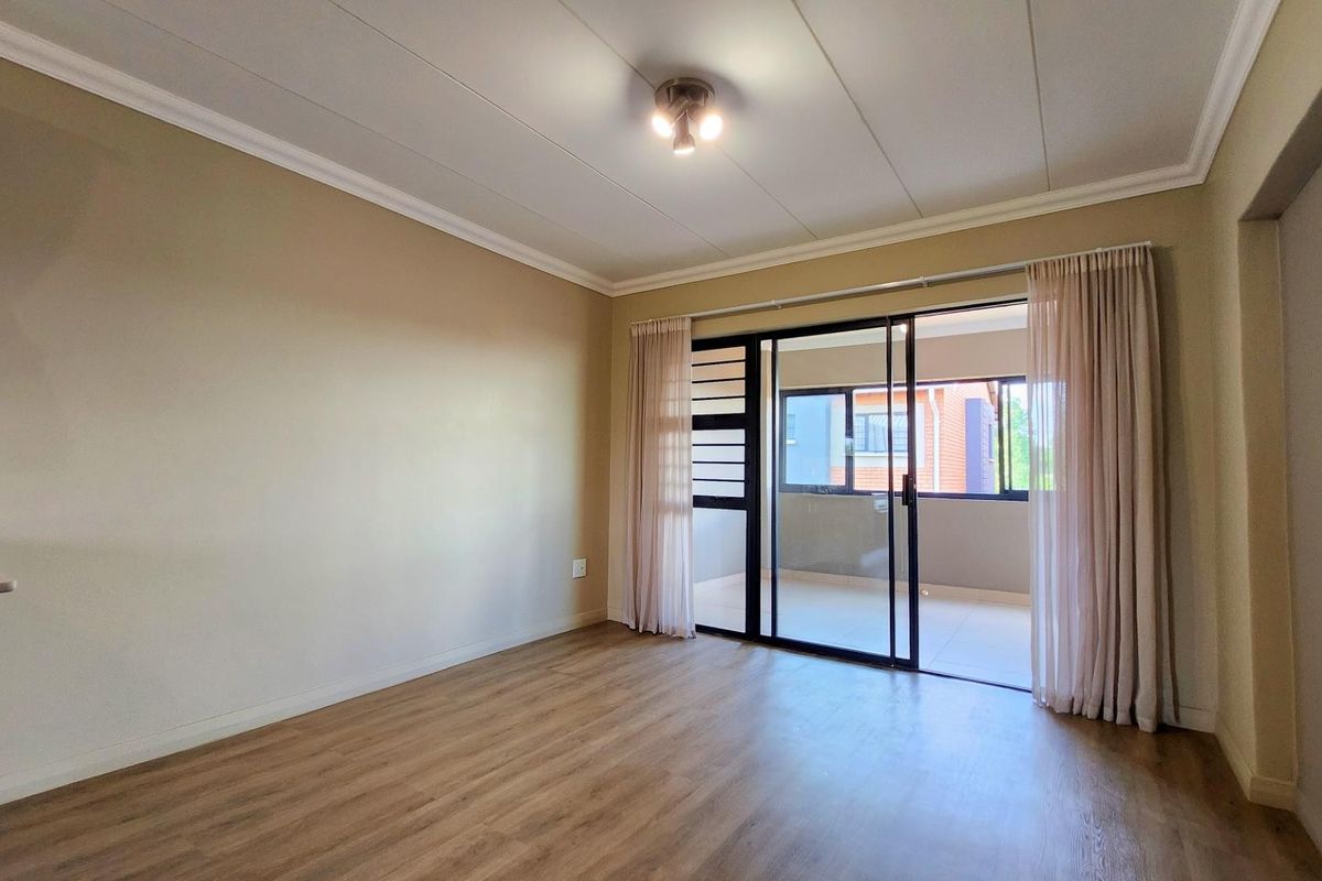 A bright, empty living room featuring laminate flooring, neutral walls, and a sliding glass door leading to an outdoor balcony area.
