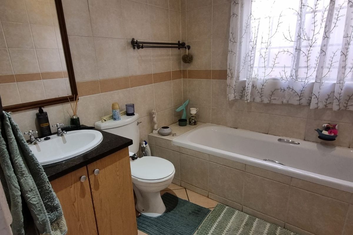A functional bathroom featuring a built-in vanity with basin, a standard toilet, and a tiled bathtub surround with neutral wall tiling.