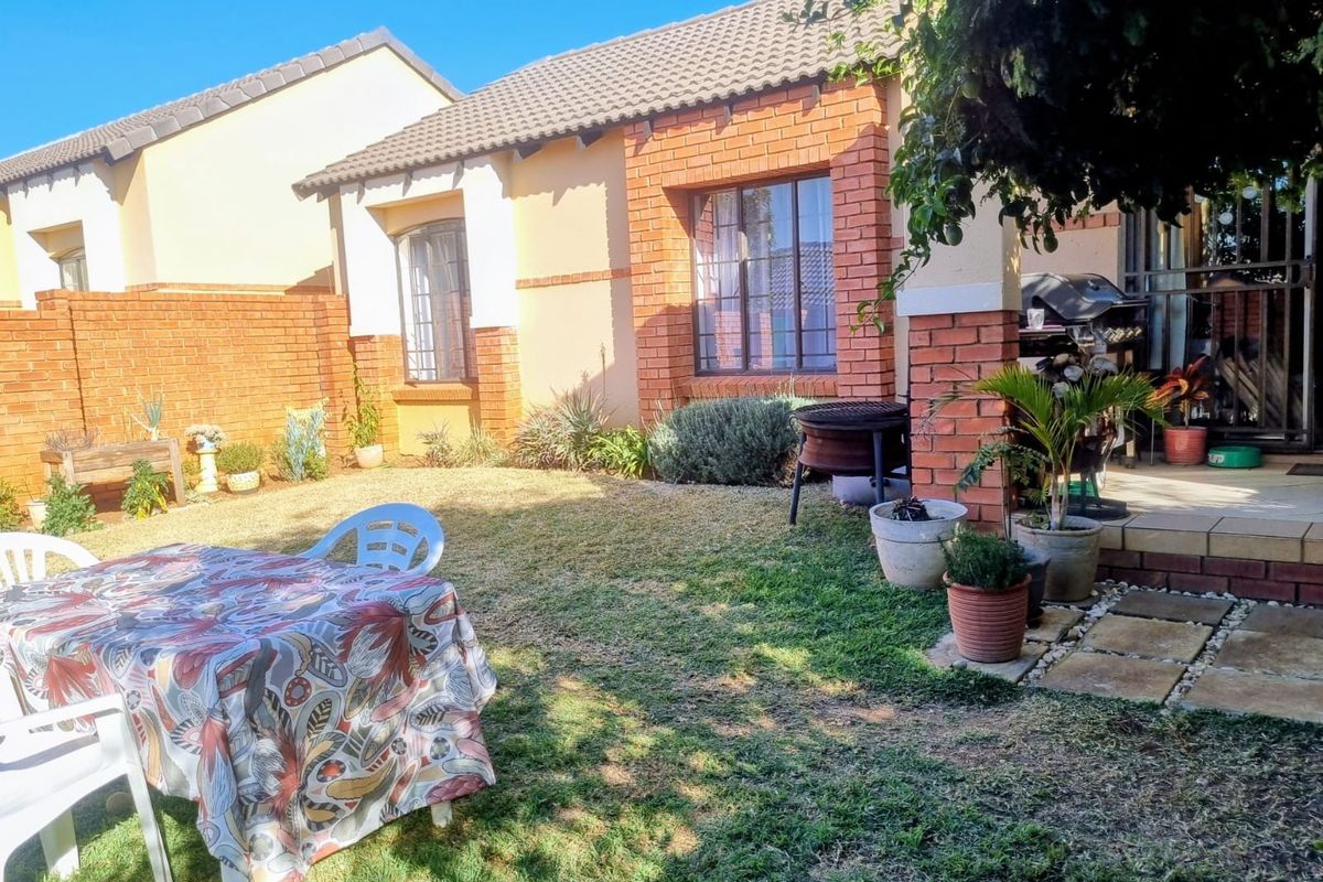 A private rear garden featuring a paved patio area, established lawn, and brick-accented townhouse facade with tiled roofing.
