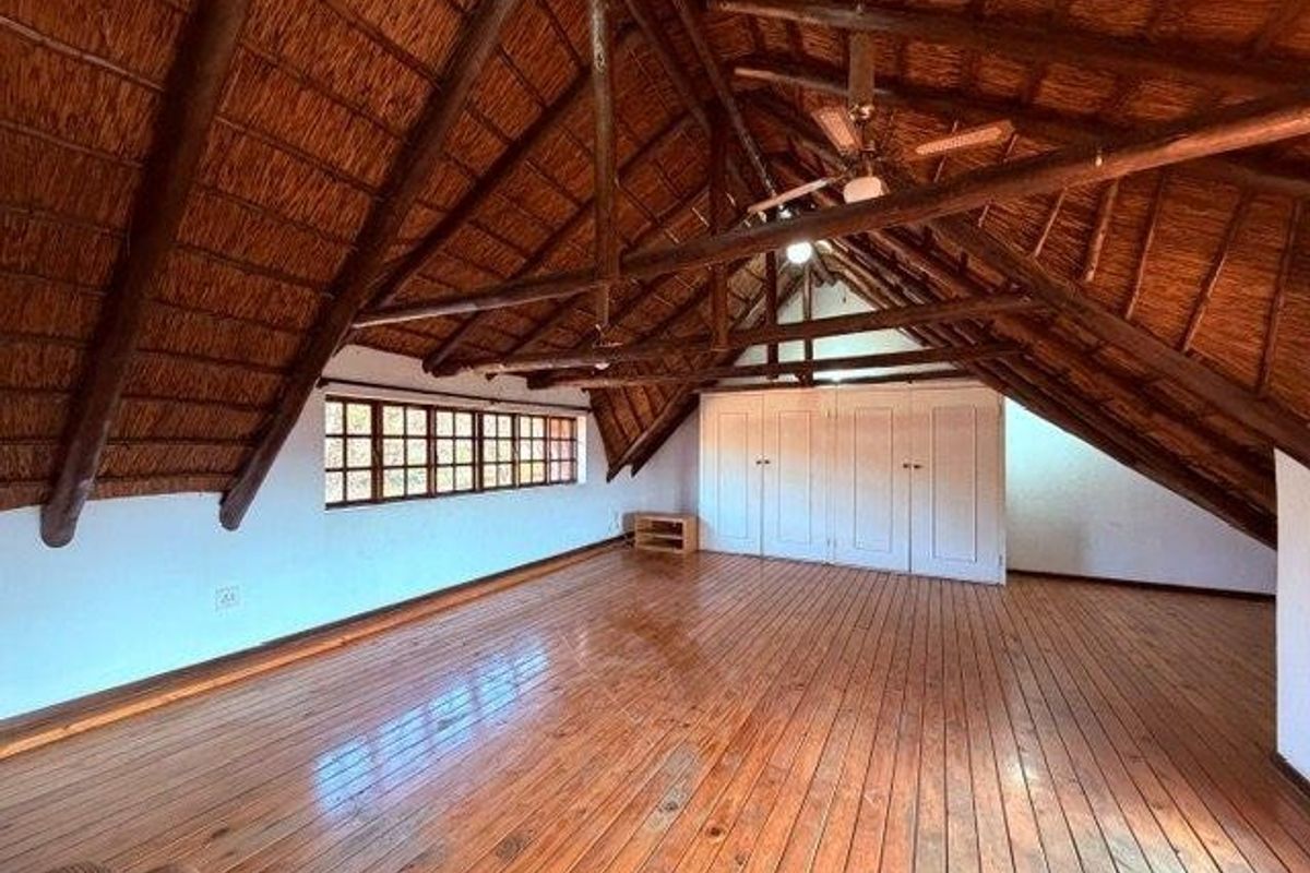 Spacious loft bedroom featuring exposed timber rafters, a traditional thatched roof, polished timber flooring, and ample built-in cupboard storage.