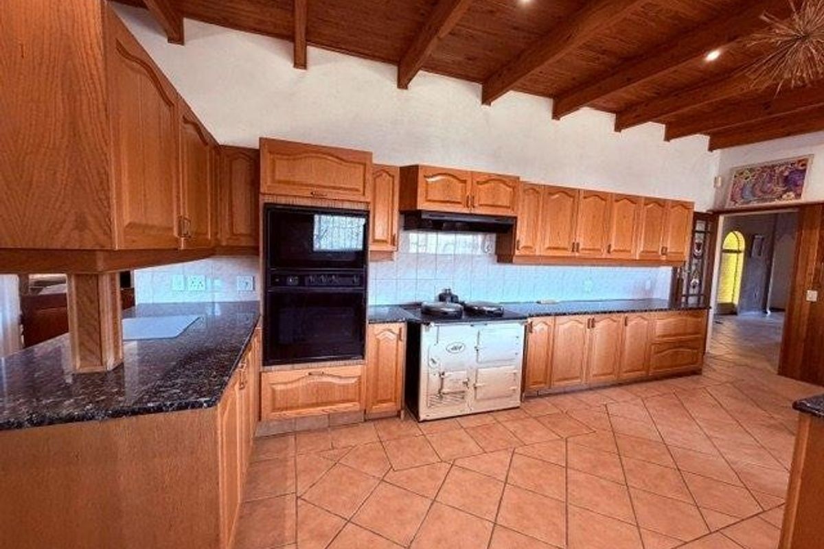 Spacious kitchen featuring timber cabinetry, granite countertops, a built-in double oven, range cooker, and exposed timber beam ceilings with tiled flooring.