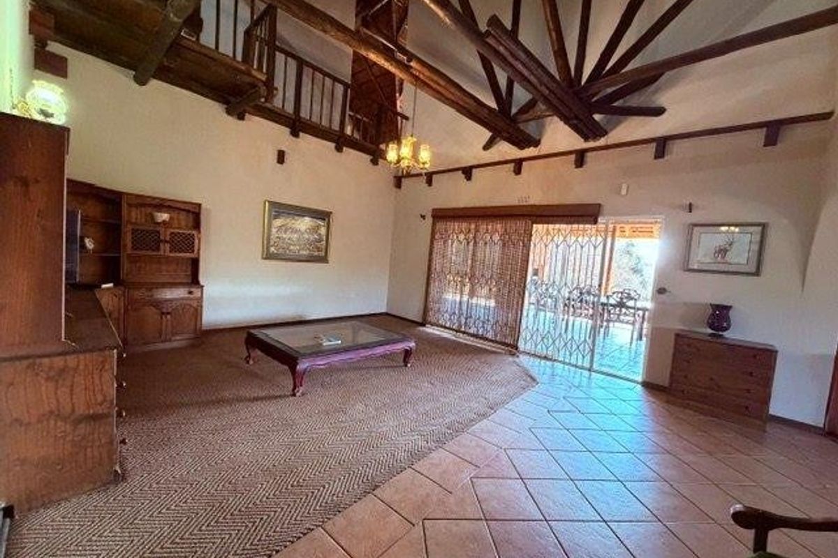 Spacious living area featuring high vaulted ceilings with exposed timber trusses, a mezzanine level, terracotta flooring, and direct access to an outdoor patio.