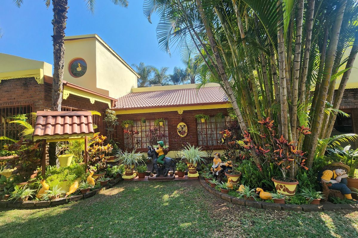 A well-maintained rear garden area featuring a brick-clad house exterior, tiled roofing, and established tropical landscaping.