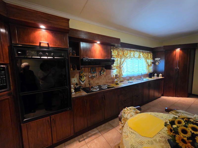 A traditional kitchen featuring extensive dark wood cabinetry, integrated oven, electric hob, and tiled flooring, offering a classic aesthetic with ample storage space.