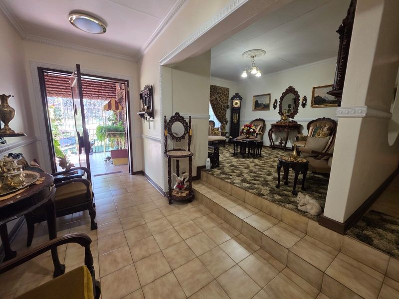 Entrance foyer with tiled flooring leading to a raised living area, featuring decorative ceiling cornices and a classic architectural layout.