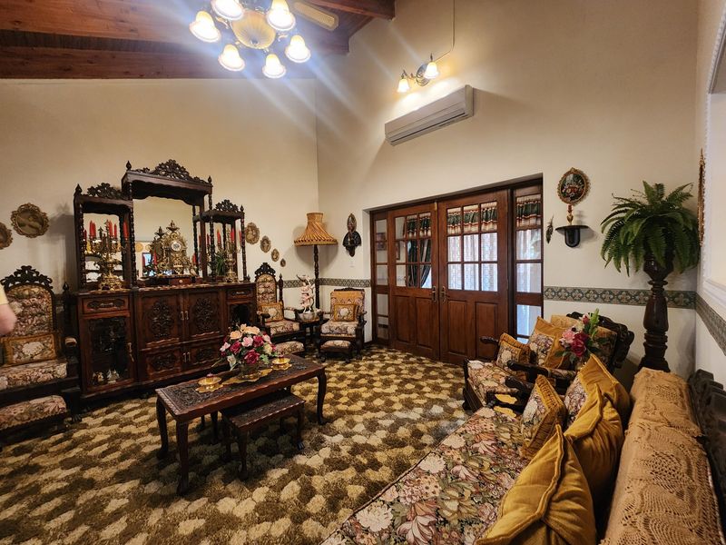 A spacious living room featuring exposed timber ceiling beams, a split-system air conditioner, and timber-framed glass panel doors leading to an adjoining area.