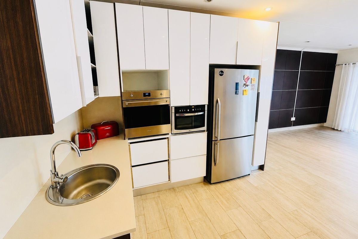 Modern kitchen featuring white high-gloss cabinetry, integrated stainless steel appliances, and a sleek sink area, seamlessly flowing into the adjacent living space.
