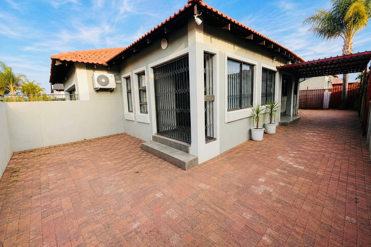 Rear exterior view of the house featuring a paved driveway, terracotta roof tiles, security gates, and a covered carport area.