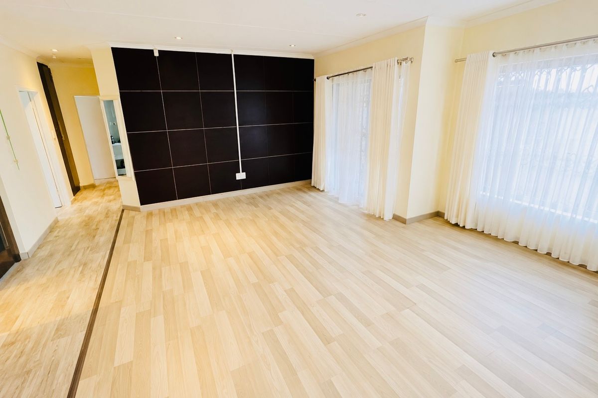 A bright and spacious living area featuring light wood-look laminate flooring, a dark feature wall, and large windows with installed curtain tracks.