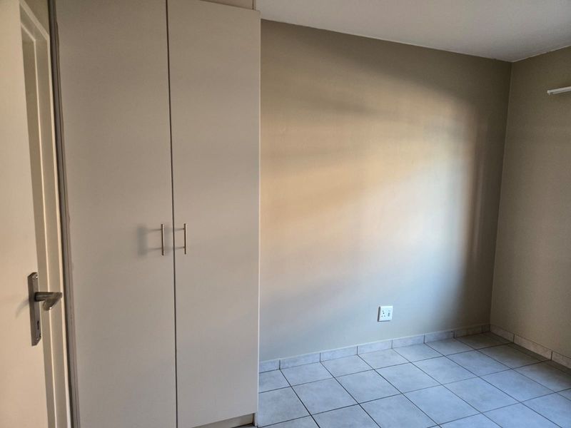 A clean, empty bedroom featuring neutral wall tones, tiled flooring, and a functional built-in wardrobe.