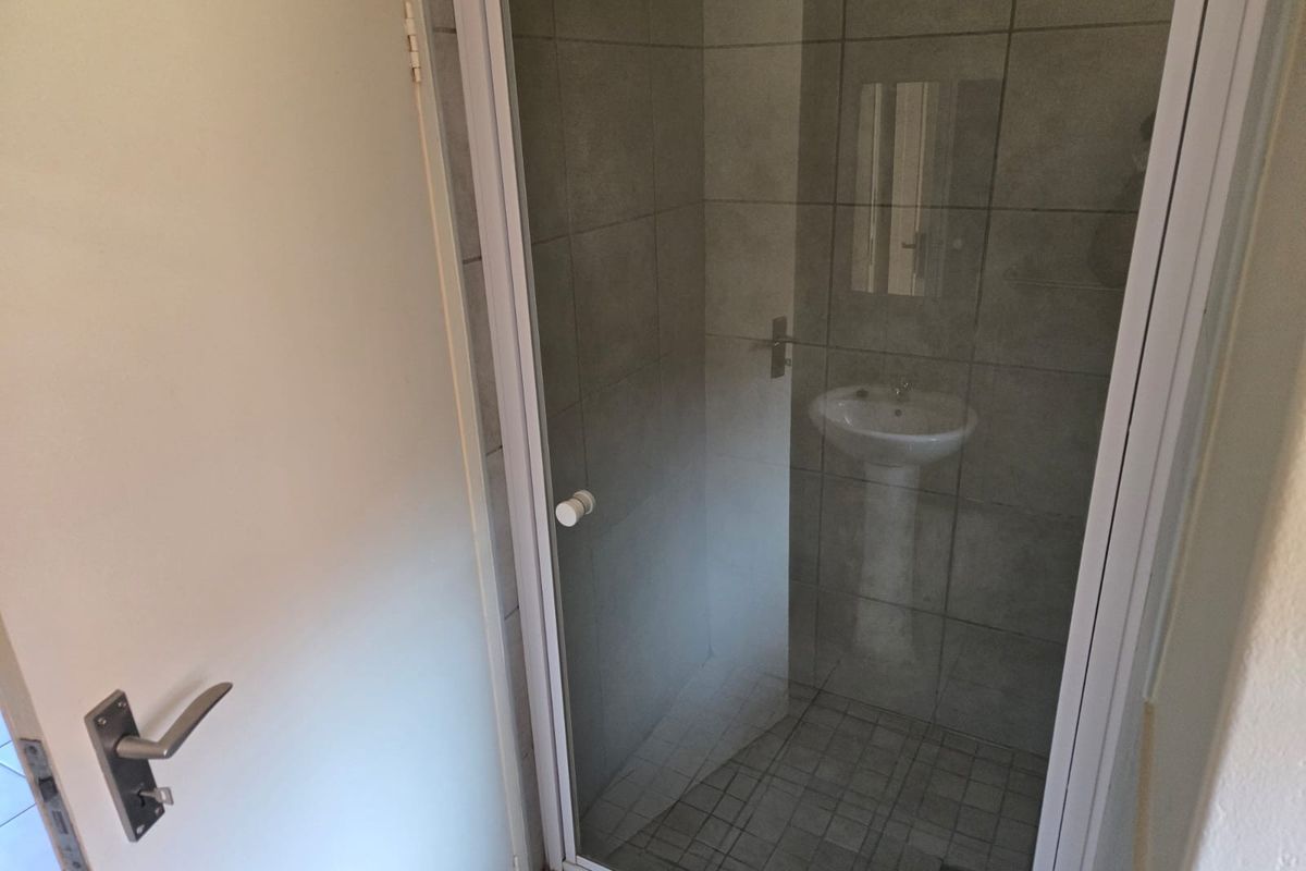 A compact bathroom featuring a pedestal basin and a glass-enclosed shower with neutral grey wall and floor tiling.