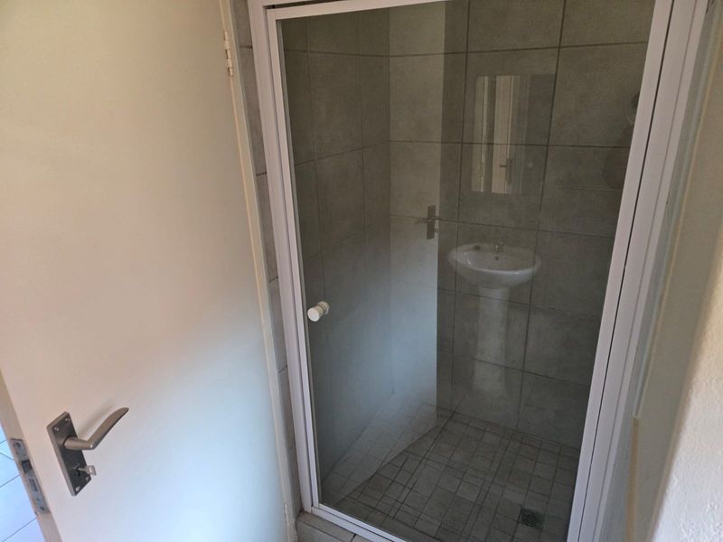 A compact bathroom featuring a pedestal basin and a glass-enclosed shower with neutral grey wall and floor tiling.