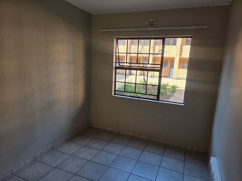 An empty bedroom featuring tiled flooring, a metal-framed window with security bars, and neutral wall finishes.