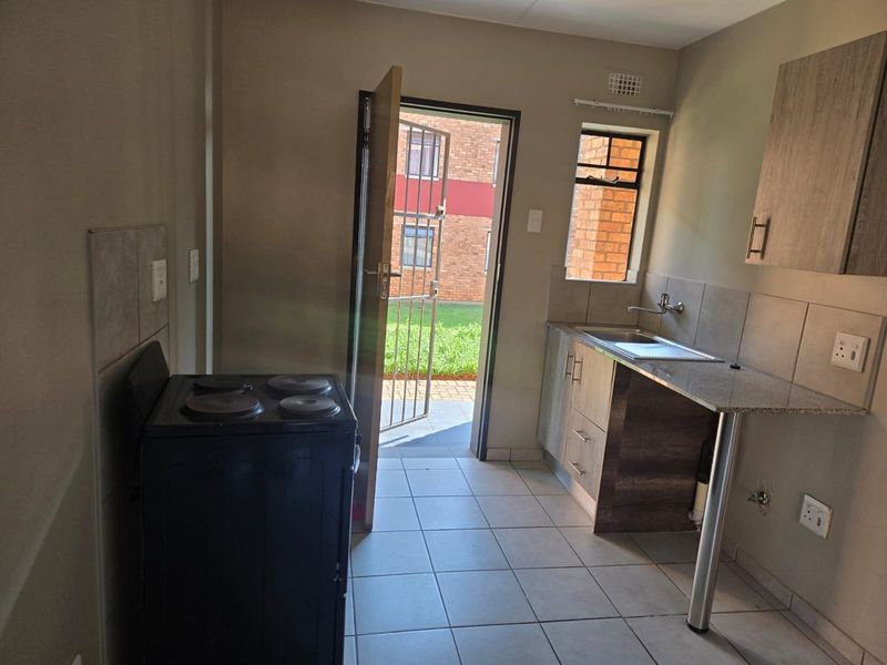 A functional kitchen featuring tiled flooring, granite countertops, built-in cabinetry, and direct access to an outdoor area through a security gate.