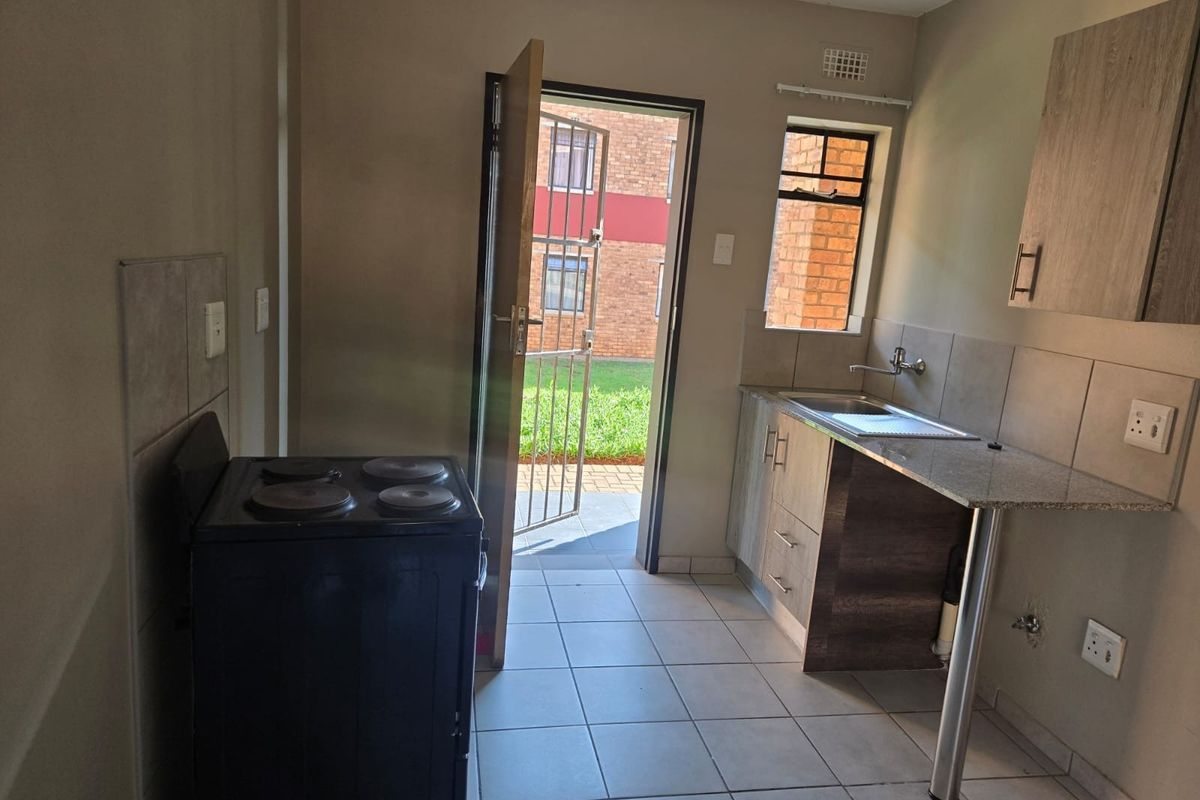 A functional kitchen featuring tiled flooring, granite countertops, built-in cabinetry, and direct access to an outdoor area through a security gate.