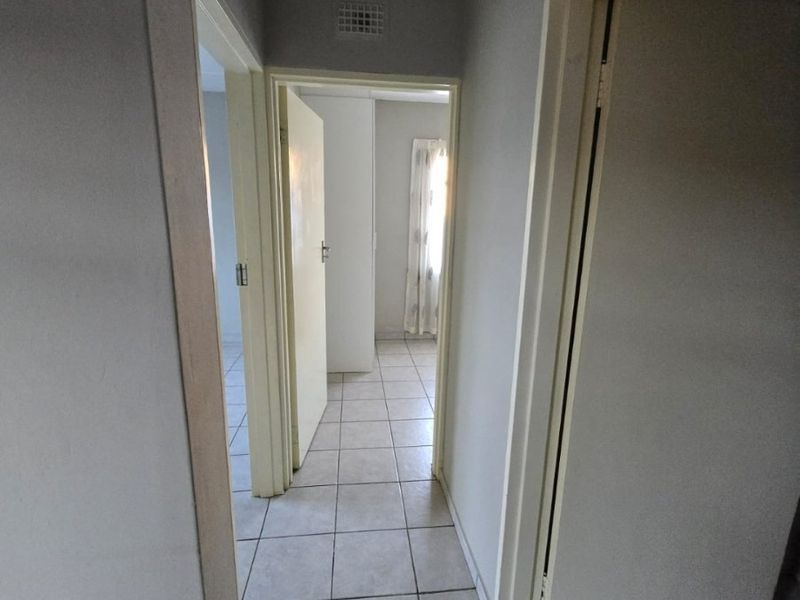 A functional hallway featuring neutral ceramic floor tiles and access to multiple rooms within the apartment.