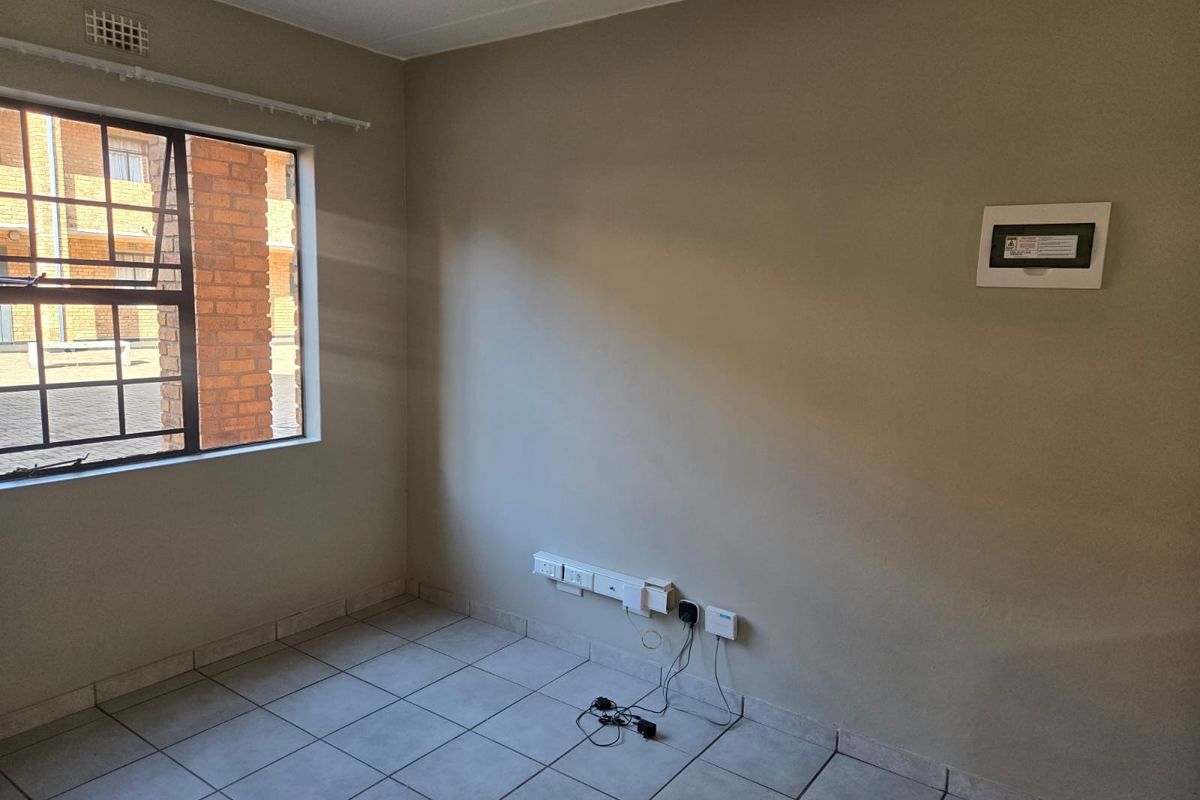 An empty bedroom featuring neutral wall paint, tiled flooring, and a steel-framed window with security bars.