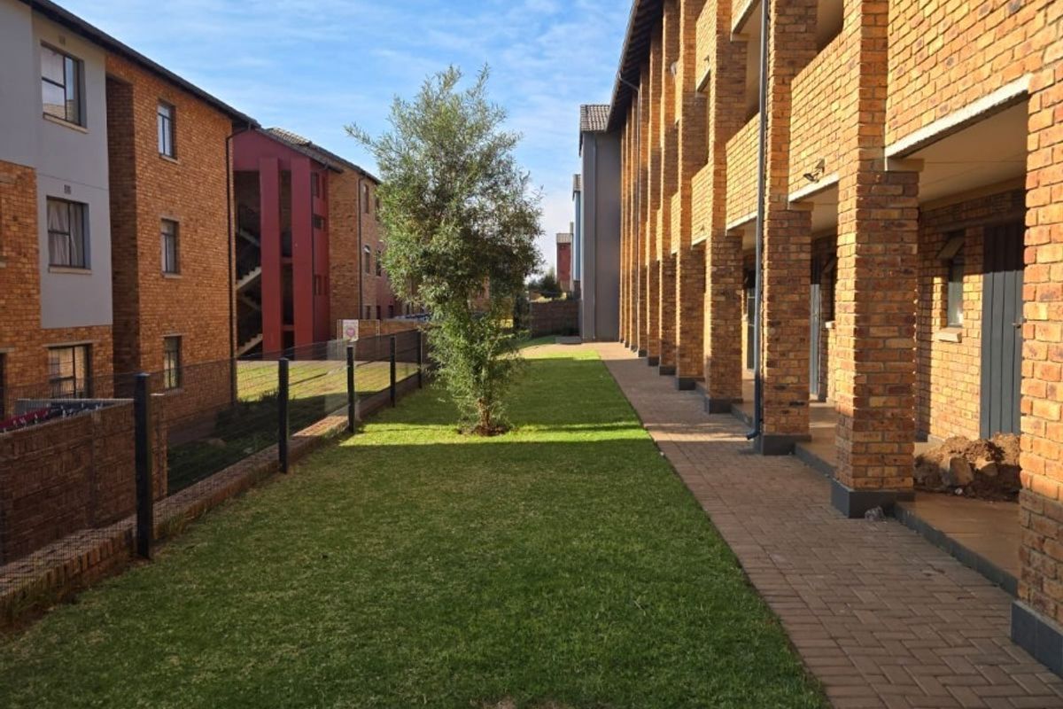 A view of the rear exterior of the apartment complex, featuring a brick facade, a paved walkway, and a shared lawn area.