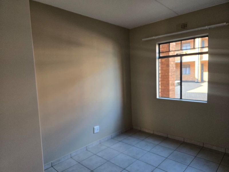 An empty bedroom featuring neutral wall paint, tiled flooring, and a window with a metal frame.