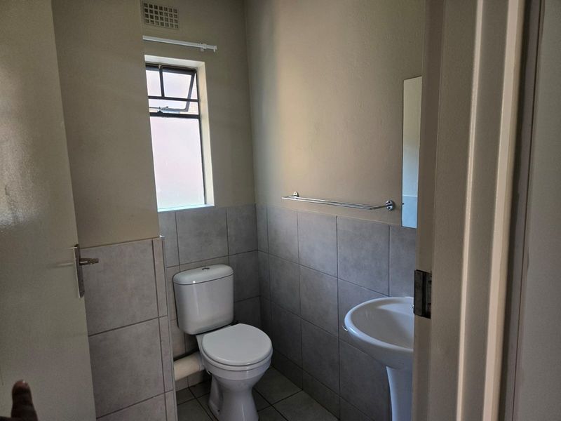 A clean, functional bathroom featuring a pedestal basin, toilet, and neutral wall and floor tiling.