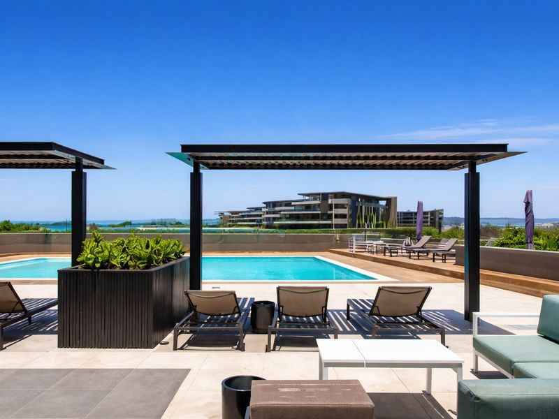 A well-maintained outdoor pool area featuring a swimming pool, timber decking, tiled patio, and modern metal pergolas with scenic views.