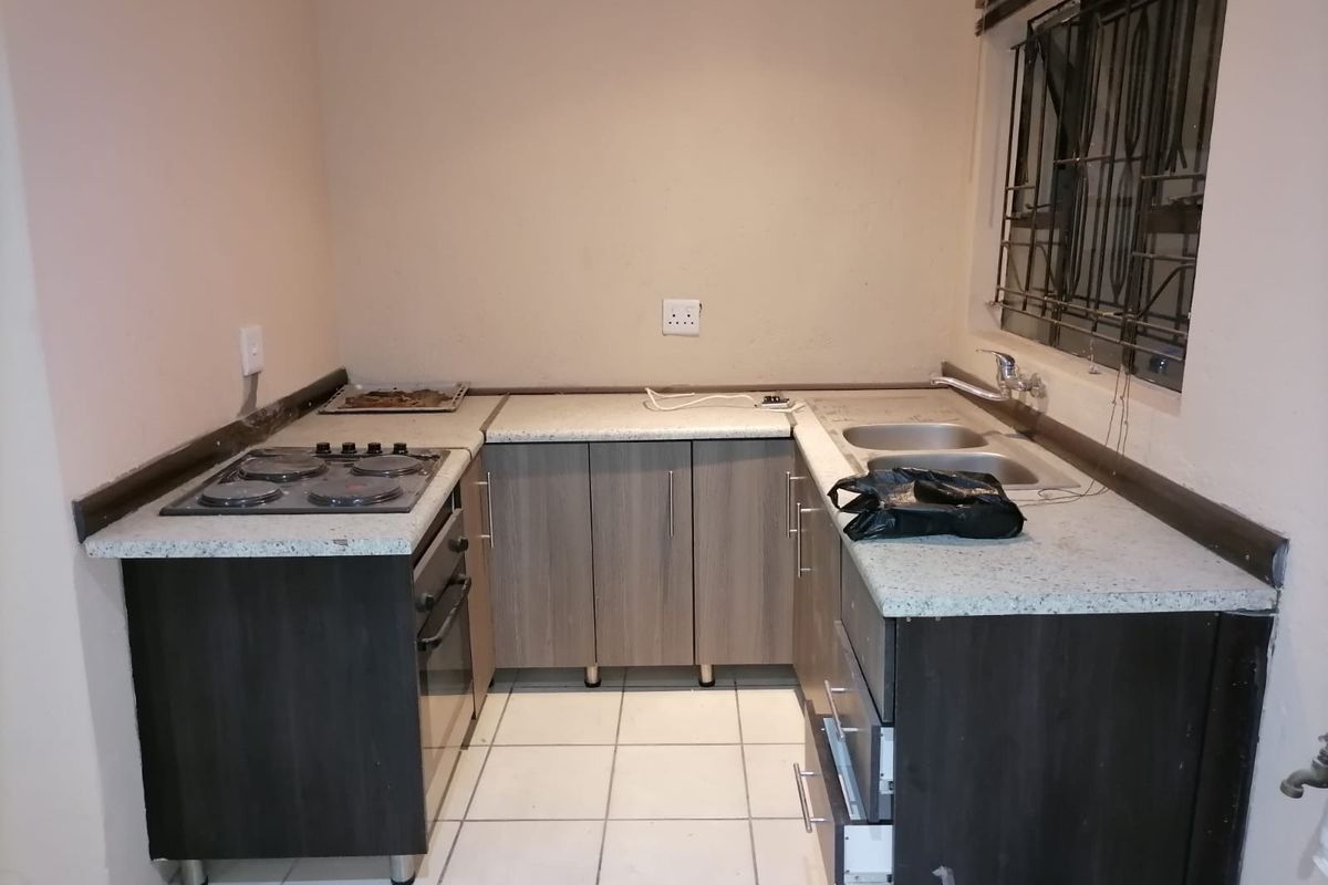 Compact kitchen featuring built-in oven, electric hob, double sink, and laminate cabinetry with stone-look countertops.
