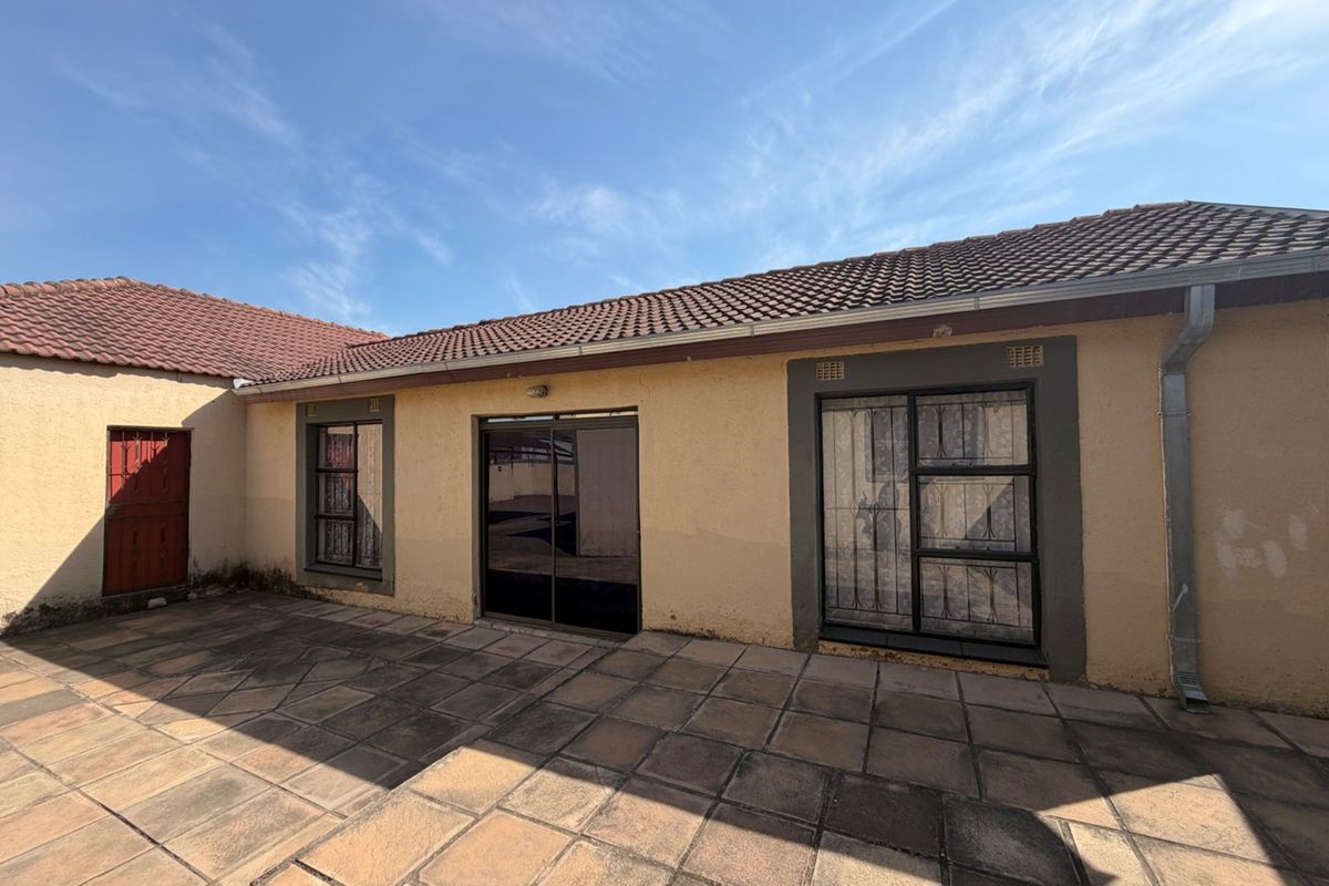 Rear exterior view of the property featuring a paved patio area, sliding glass door access, and security-fitted windows under a tiled roof.
