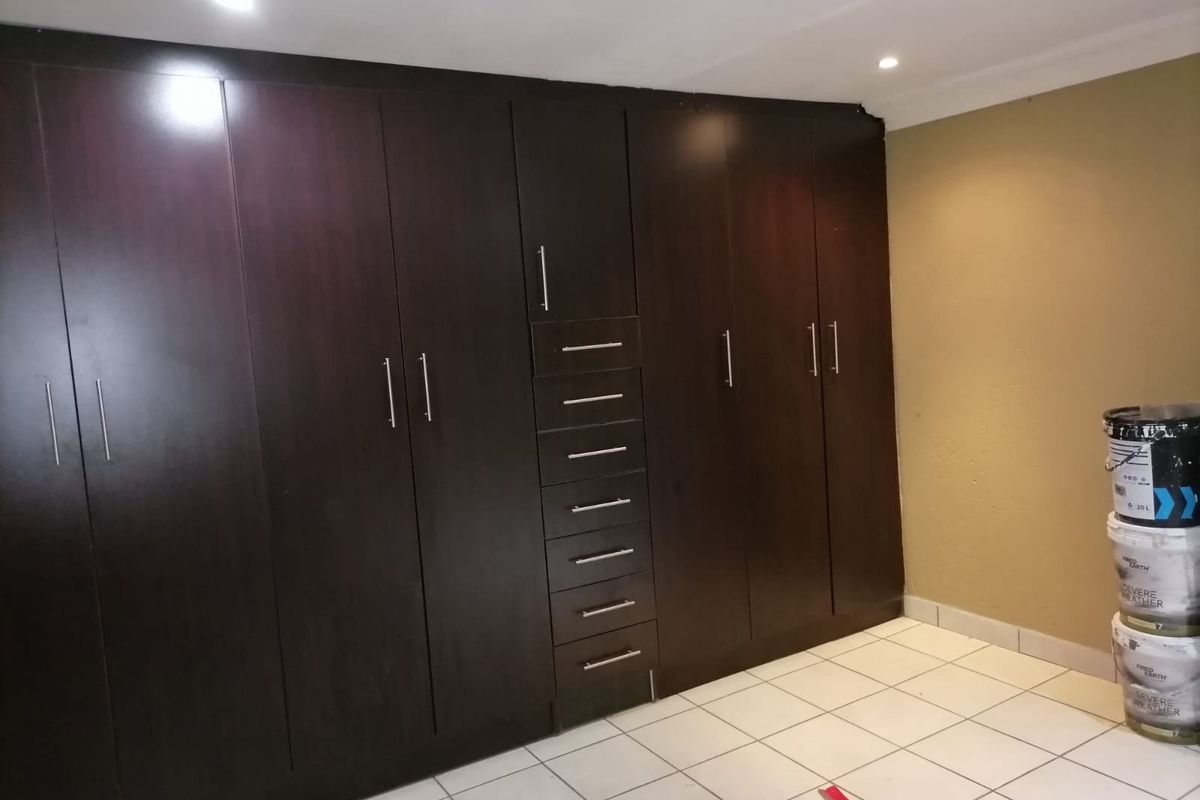 A bedroom featuring extensive dark wood built-in cupboards, tiled flooring, and recessed ceiling lighting.