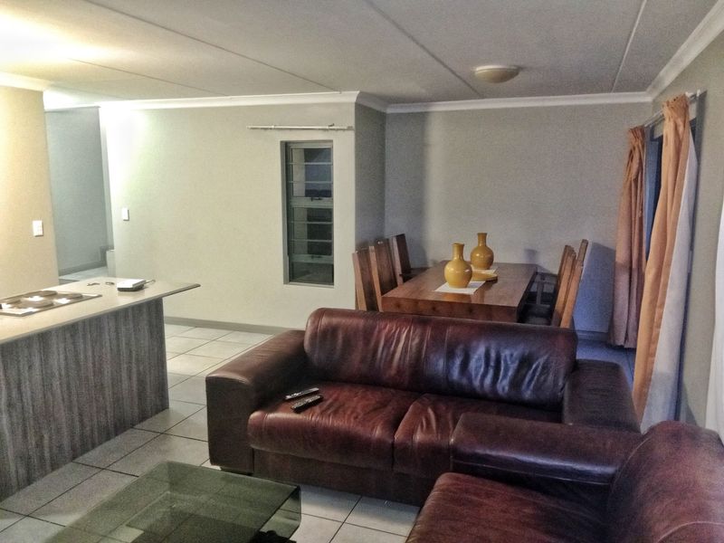 Open-plan living and dining area featuring tiled flooring, a kitchen island with a built-in hob, and neutral wall finishes.