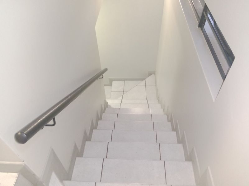 A clean, minimalist staircase featuring white tiled steps and a sturdy metal handrail, providing a bright and modern transition between levels.