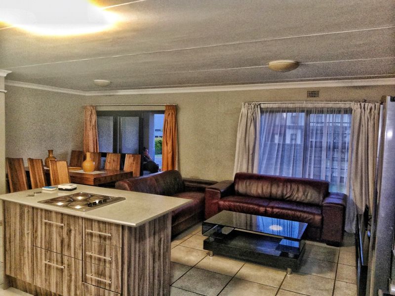 Open-plan living and dining area featuring a kitchen island with a built-in hob, tiled flooring, and sliding glass doors leading to the exterior.