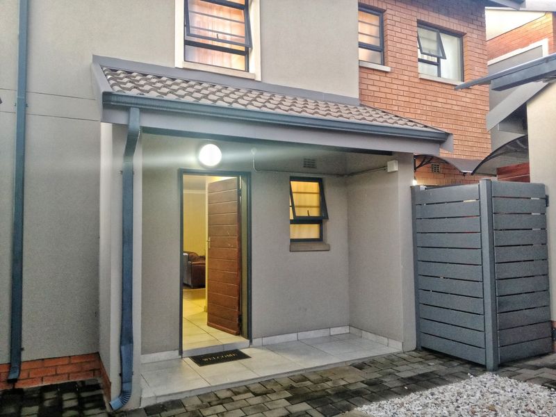 Front entrance area featuring a covered tiled porch, timber door, and modern grey exterior finishes with paved access.