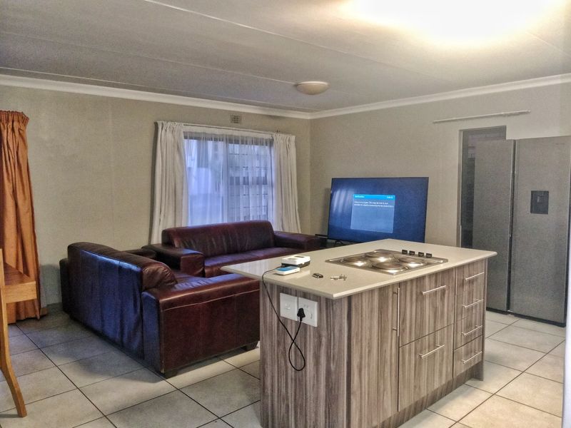 Open-plan living area featuring a central kitchen island with a built-in hob and tiled flooring throughout.