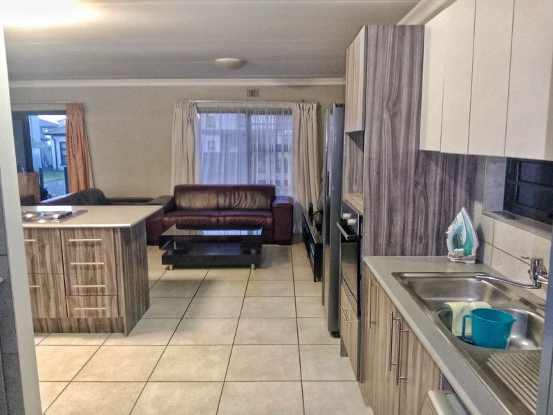 Open-plan living area featuring a modern kitchen with laminate cabinetry, a central island, and tiled flooring, seamlessly flowing into the adjacent lounge space.