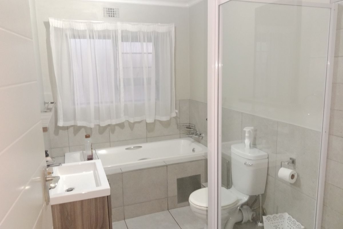 A functional bathroom featuring a built-in bathtub, separate shower enclosure, toilet, and a modern vanity basin with neutral wall and floor tiling.