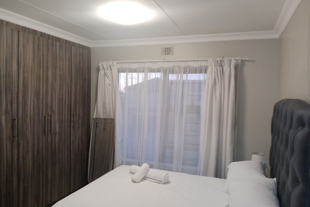 A well-maintained bedroom featuring floor-to-ceiling built-in cupboards, decorative ceiling cornicing, and a ventilation grille.