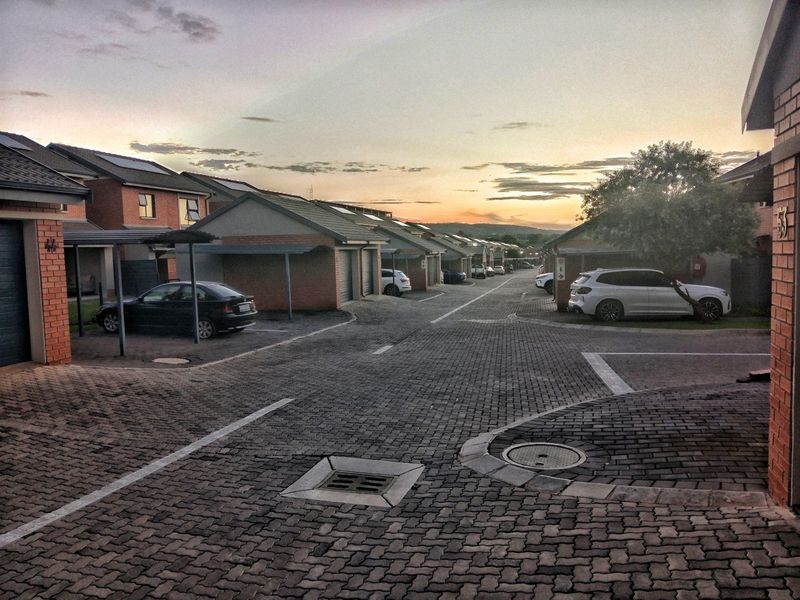 A view of a residential complex street featuring paved driveways, brick-faced homes, and covered parking structures at sunset.