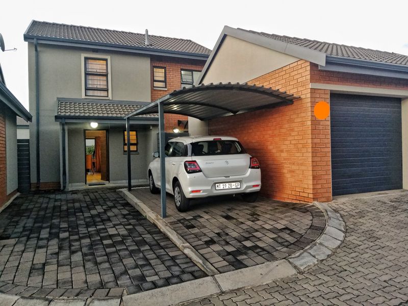 Front exterior view featuring a paved driveway, a covered carport, and an attached garage with a modern sectional door.