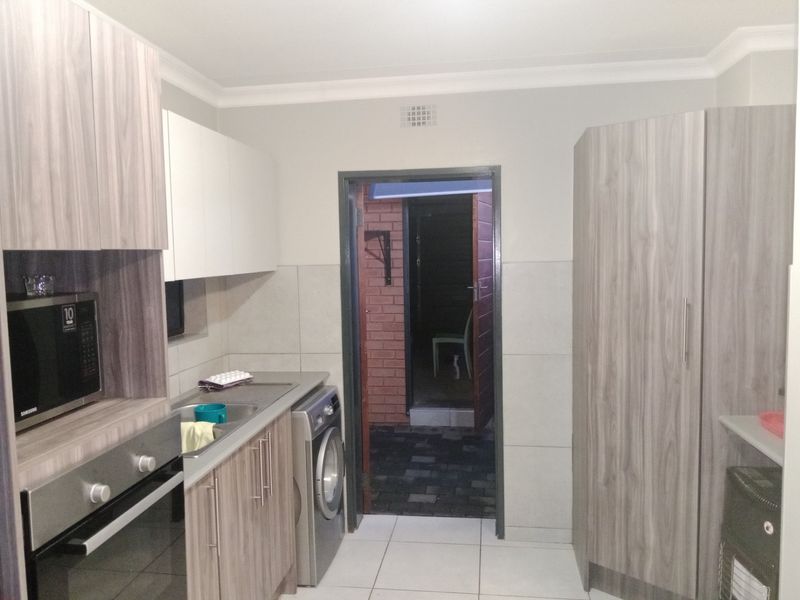 A modern kitchen featuring wood-grain cabinetry, built-in oven, microwave, and tiled flooring, with direct access to an exterior area.