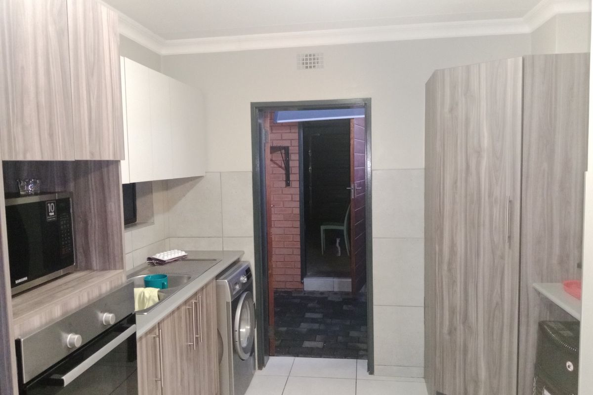 A modern kitchen featuring wood-grain cabinetry, built-in oven, microwave, and tiled flooring, with direct access to an exterior area.